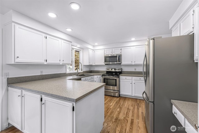 kitchen with a peninsula, light wood-style flooring, a sink, appliances with stainless steel finishes, and white cabinetry