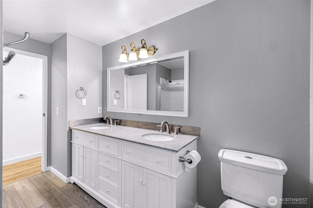 bathroom with double vanity, toilet, wood finished floors, and a sink