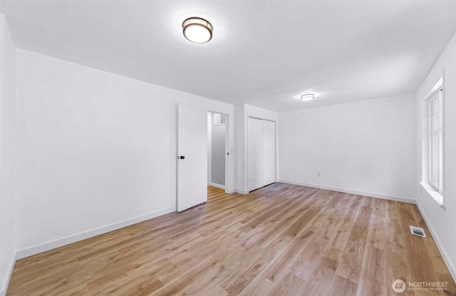 spare room with light wood-type flooring, visible vents, and baseboards