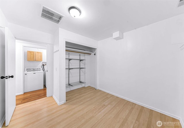 unfurnished bedroom with washer / dryer, light wood-style flooring, visible vents, and a closet