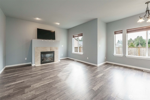 unfurnished living room featuring dark wood-style floors, a notable chandelier, a tiled fireplace, and baseboards