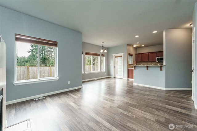 unfurnished living room with visible vents, a notable chandelier, dark wood-style floors, recessed lighting, and baseboards