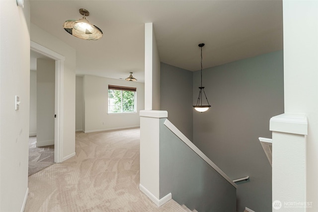 hallway with baseboards, an upstairs landing, and light carpet