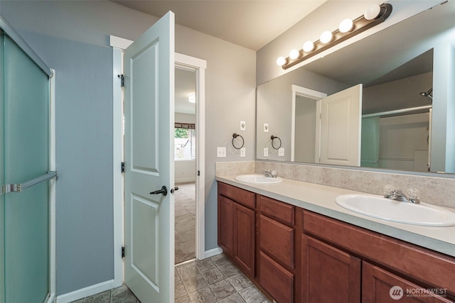 bathroom with a shower with door, double vanity, baseboards, and a sink