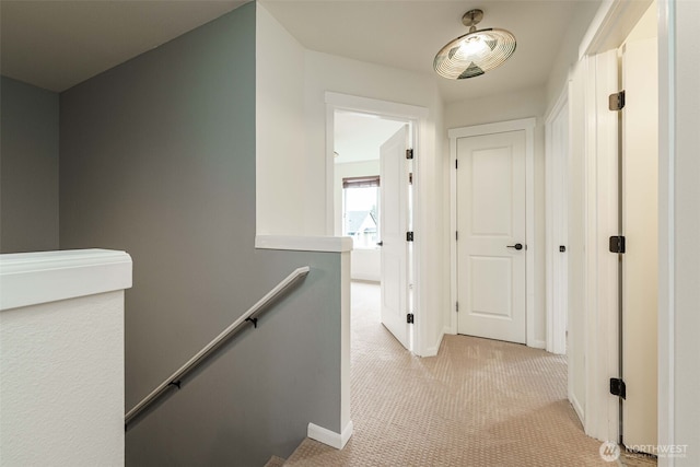 hallway with an upstairs landing, light carpet, and baseboards