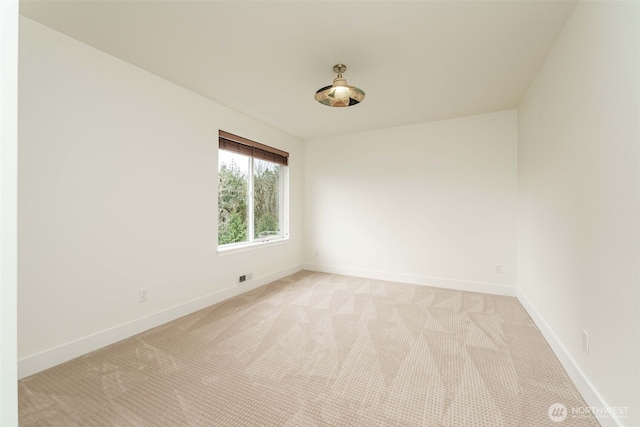 spare room featuring light colored carpet and baseboards