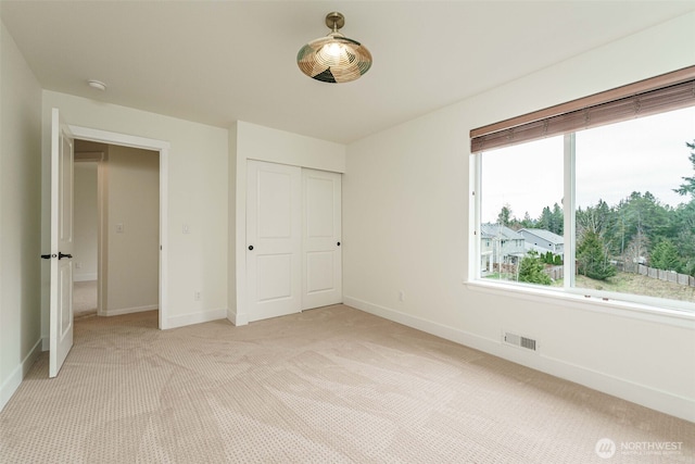 unfurnished bedroom with baseboards, visible vents, a closet, and light carpet