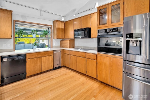 kitchen with light countertops, brown cabinets, light wood-style floors, black appliances, and a sink