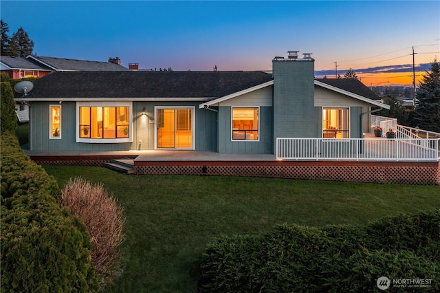 back of house at dusk featuring a wooden deck, a chimney, and a yard