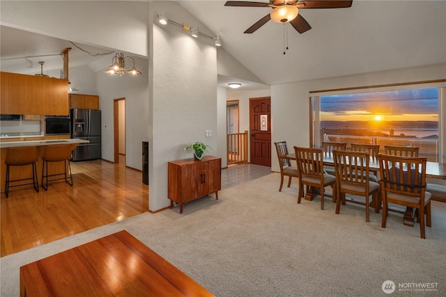 dining space with high vaulted ceiling, ceiling fan, track lighting, light wood-style floors, and light carpet