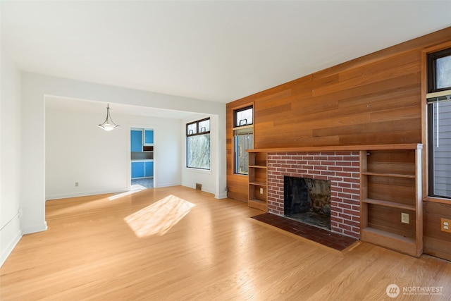 unfurnished living room with a fireplace, wood finished floors, baseboards, and wood walls