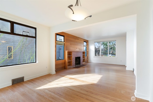 unfurnished living room with visible vents, light wood-style flooring, wood walls, baseboards, and a brick fireplace