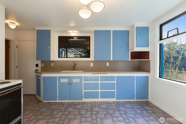 kitchen featuring backsplash, light countertops, white range with electric stovetop, blue cabinets, and a sink