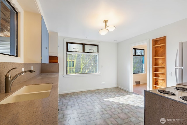 kitchen with brick floor, freestanding refrigerator, baseboards, and a sink