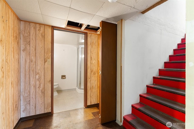 stairway featuring tile patterned floors, a drop ceiling, and wood walls