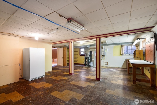 basement with a drop ceiling, heating unit, water heater, and freestanding refrigerator