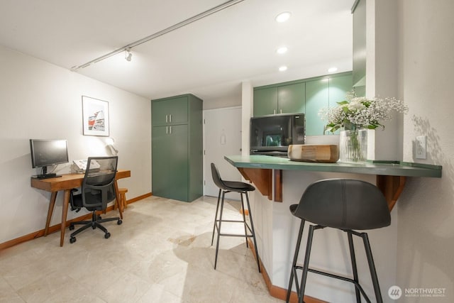 kitchen with track lighting, baseboards, a breakfast bar, a peninsula, and green cabinetry