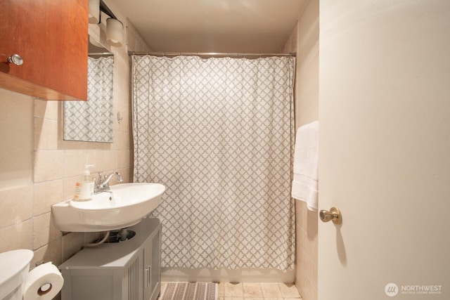 bathroom featuring a shower with shower curtain, tile walls, toilet, and a sink