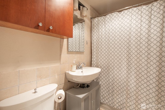 bathroom featuring a shower with shower curtain, toilet, tile walls, and a sink