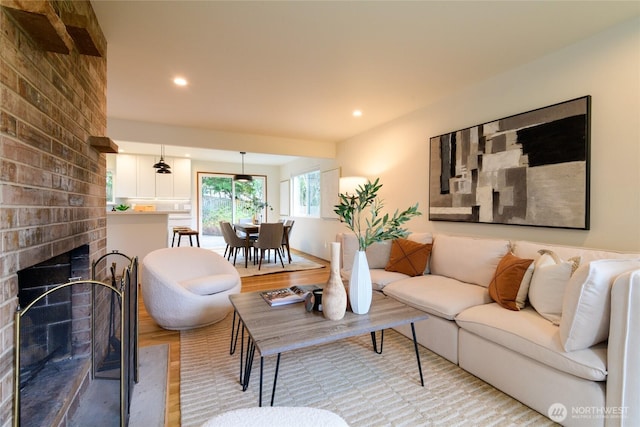 living area with a brick fireplace, recessed lighting, and light wood finished floors