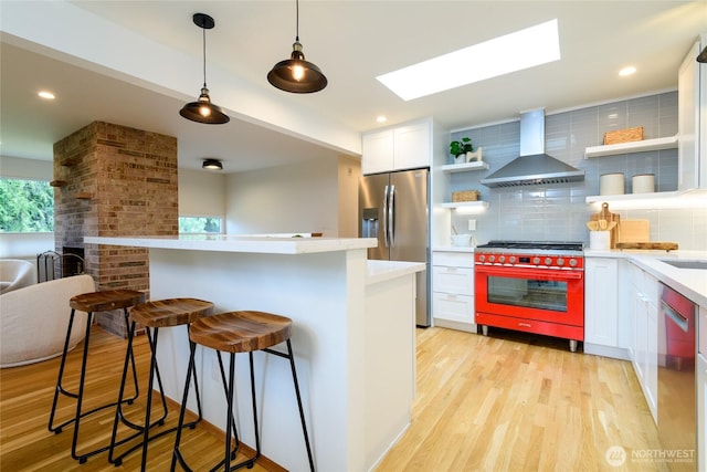 kitchen featuring open shelves, stainless steel appliances, wall chimney exhaust hood, light wood finished floors, and light countertops