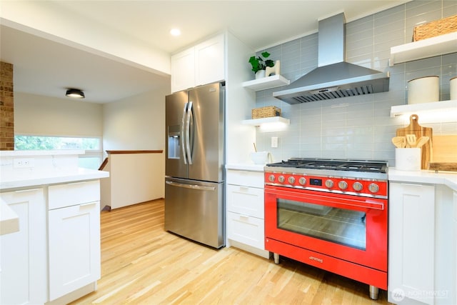 kitchen featuring open shelves, light countertops, light wood-style floors, appliances with stainless steel finishes, and wall chimney range hood