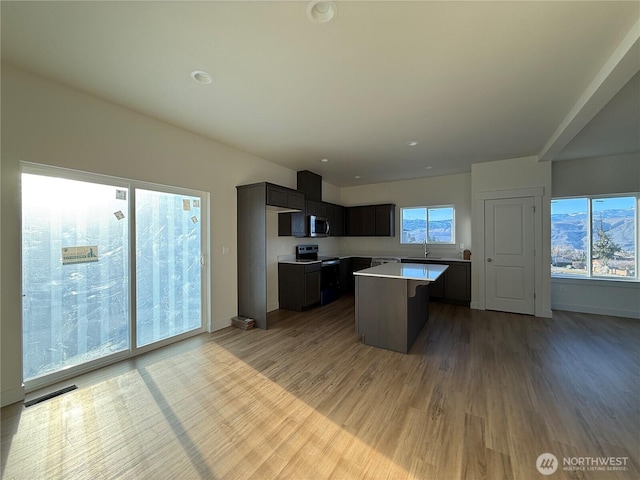 kitchen with light wood-style flooring, a sink, stainless steel appliances, light countertops, and a center island