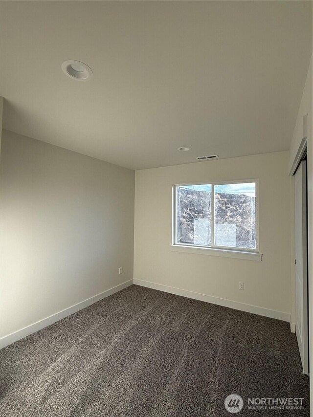 unfurnished bedroom with visible vents, dark carpet, and baseboards