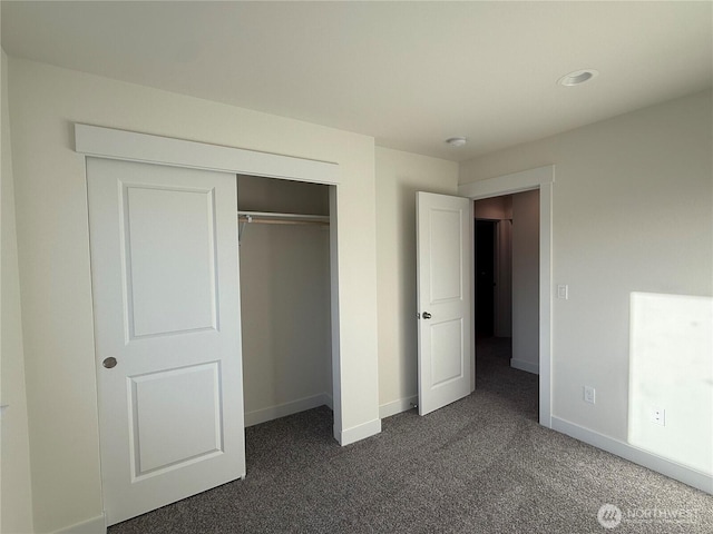 unfurnished bedroom with a closet, baseboards, and dark carpet