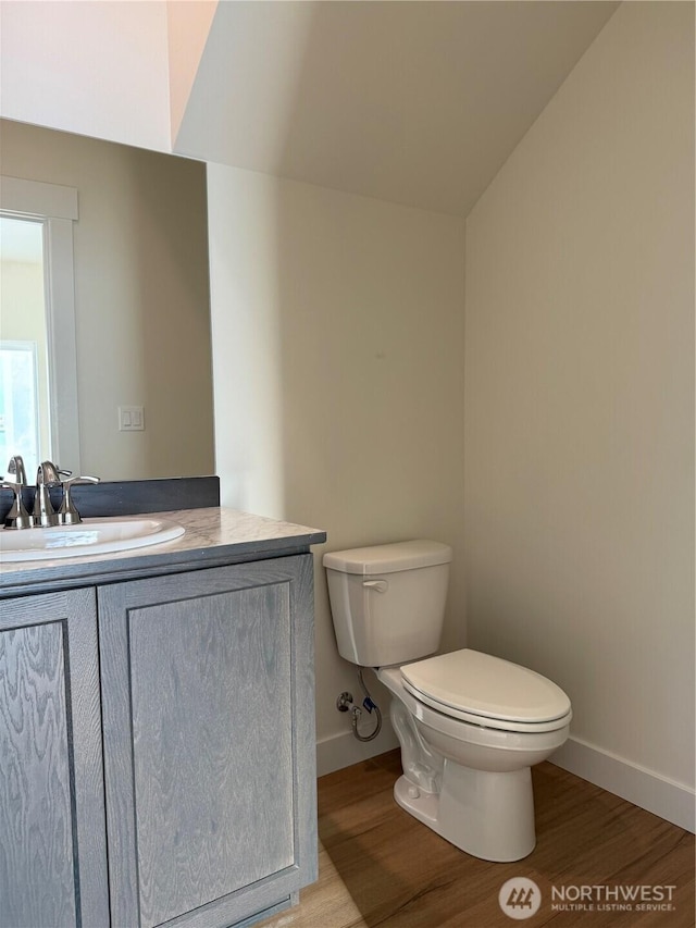 half bathroom featuring vanity, toilet, wood finished floors, and baseboards