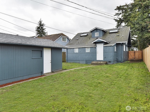 rear view of property featuring an outbuilding, a yard, fence, and a shingled roof