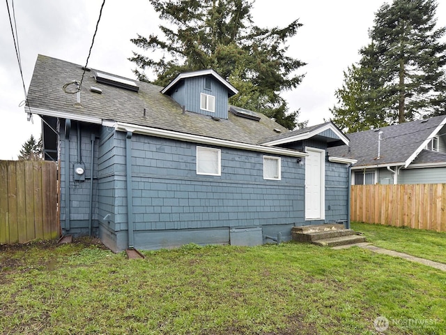 rear view of property featuring a yard, a shingled roof, and fence