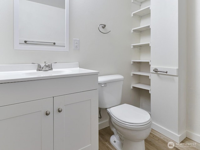 bathroom with toilet, vanity, baseboards, and wood finished floors