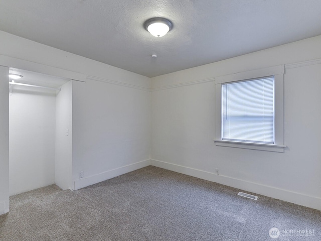 carpeted spare room with visible vents and a textured ceiling