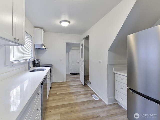 kitchen featuring visible vents, light wood finished floors, a sink, stainless steel appliances, and white cabinets