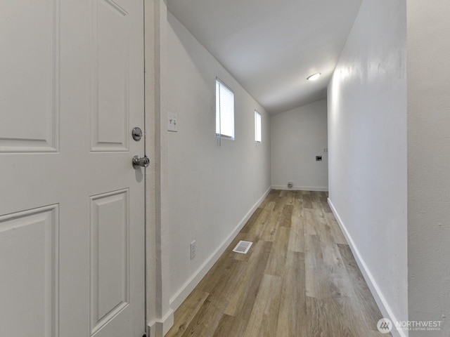 hall with light wood-style floors, baseboards, visible vents, and vaulted ceiling