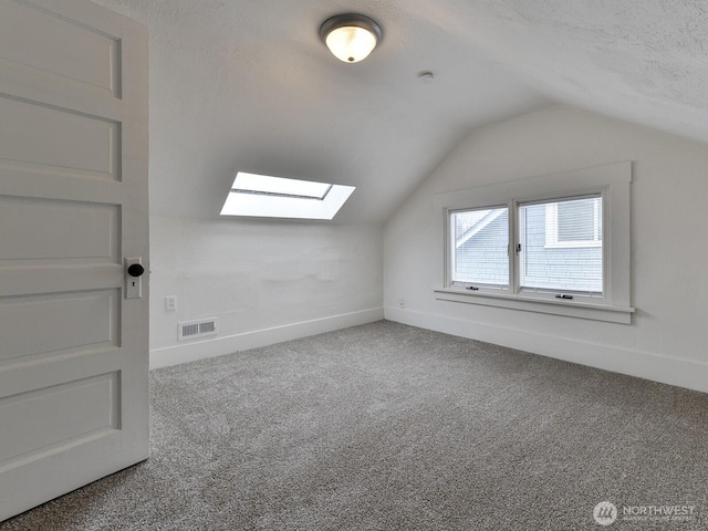 additional living space with baseboards, visible vents, carpet floors, a textured ceiling, and lofted ceiling with skylight