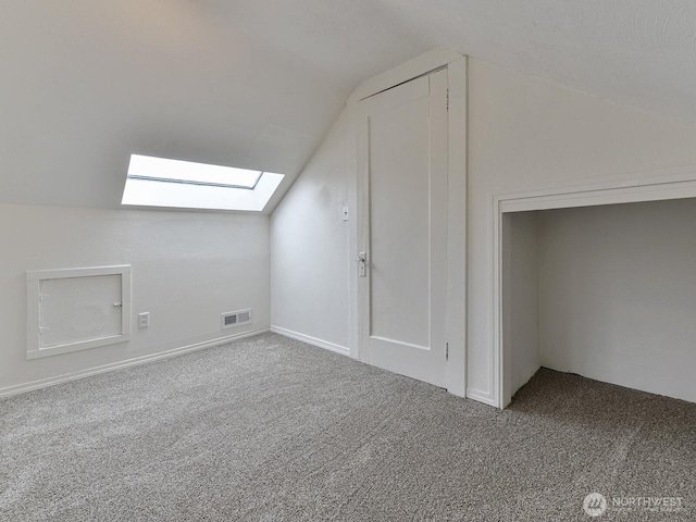 additional living space with visible vents, lofted ceiling with skylight, and carpet flooring