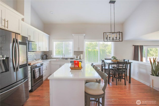 kitchen with a breakfast bar area, light countertops, decorative backsplash, appliances with stainless steel finishes, and light wood-style floors