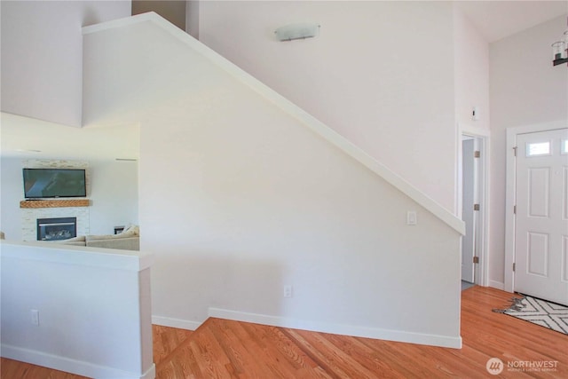 entryway with light wood-type flooring, baseboards, a glass covered fireplace, and a towering ceiling