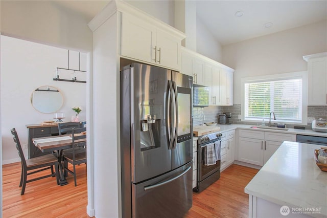 kitchen with light wood finished floors, a sink, stainless steel appliances, white cabinets, and tasteful backsplash