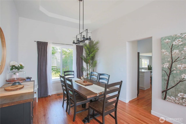 dining room with baseboards, light wood-type flooring, and a tray ceiling