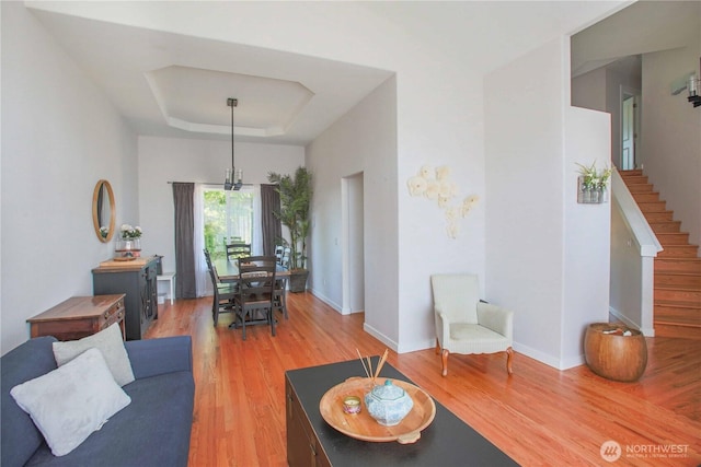 living area with light wood-type flooring, a tray ceiling, baseboards, and stairs