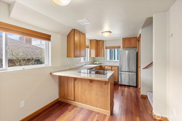 kitchen featuring black electric stovetop, light countertops, a peninsula, freestanding refrigerator, and wood finished floors