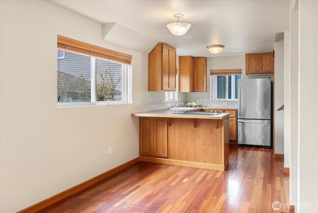 kitchen with wood finished floors, freestanding refrigerator, a peninsula, light countertops, and baseboards