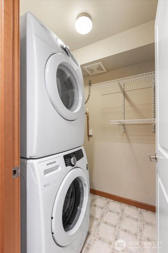 laundry room featuring baseboards, stacked washer and dryer, light floors, and laundry area