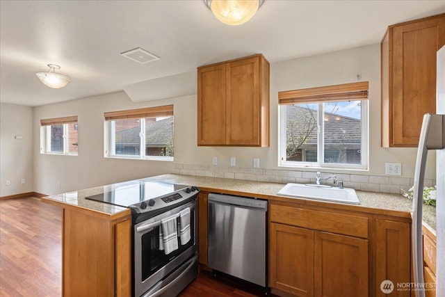 kitchen with a peninsula, a sink, stainless steel appliances, dark wood-type flooring, and brown cabinets