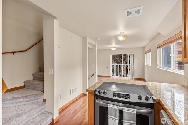 kitchen featuring electric range, baseboards, light wood-type flooring, and visible vents