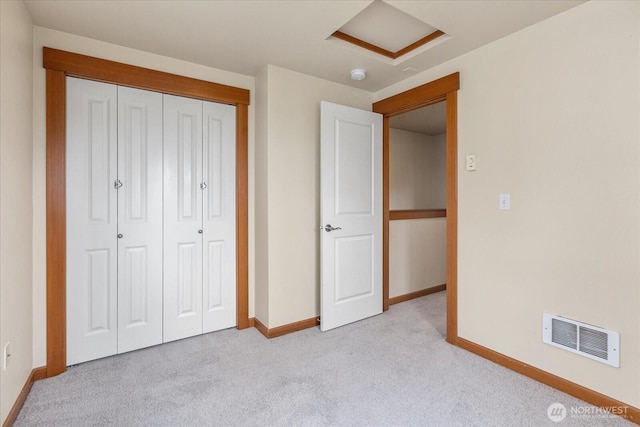 unfurnished bedroom featuring visible vents, baseboards, attic access, a closet, and light colored carpet