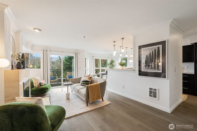 living room with heating unit, crown molding, baseboards, and wood finished floors